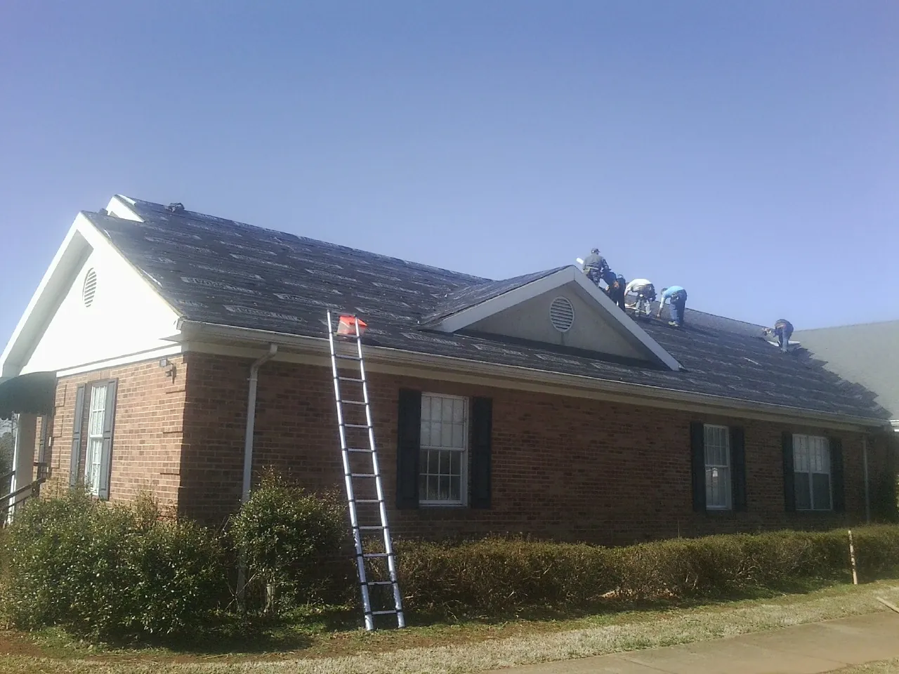 Crew tearing shingles off a brick ranch roof with a ladder set — Metal Roof Repair work by our crew in Adams