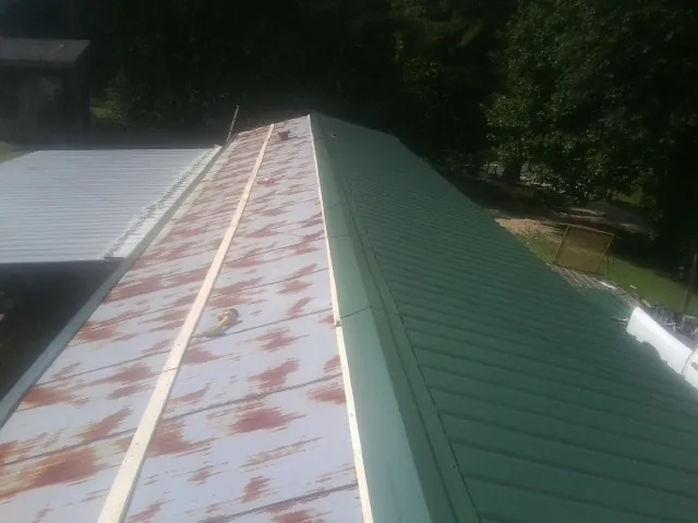 Old rusted panels beside newly installed green metal roofing — Wind Damage Roof Repair by Roofing Brothers in Adams